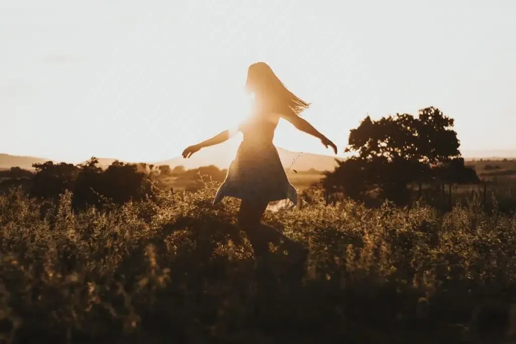 Woman walking through a sunlit field at golden hour representing happiness and wellbeing