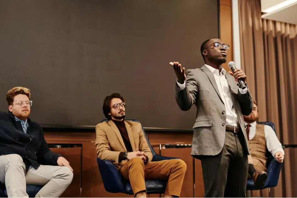 Keynote speaker presenting on stage at a business conference panel while holding a microphone and addressing an audience.