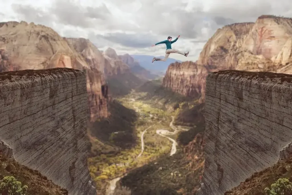 Person leaping across a dramatic canyon gap between two cliffs, symbolizing courage, risk-taking, and bold decision-making.