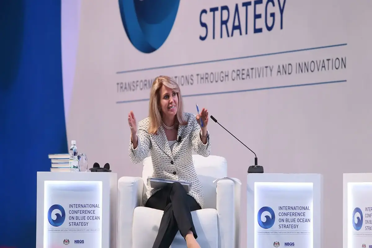 Renée Mauborgne speaking at a Blue Ocean Strategy conference, seated on stage addressing an audience on innovation and strategy