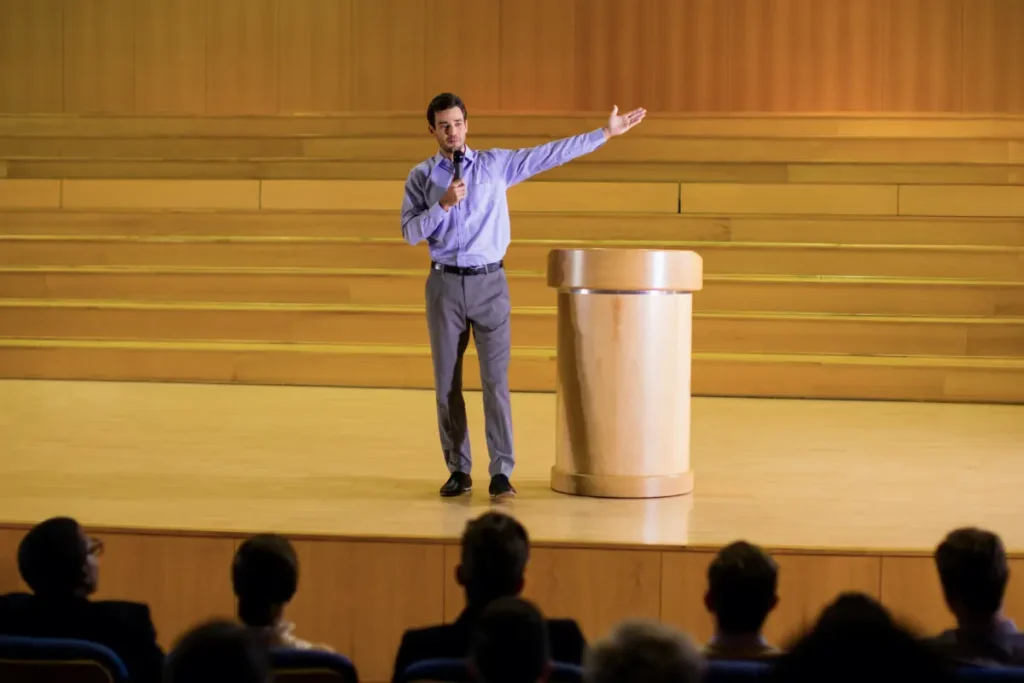 Speaker on stage gesturing to audience at a corporate event - how to introduce a keynote speaker | Aurum Speakers Bureau